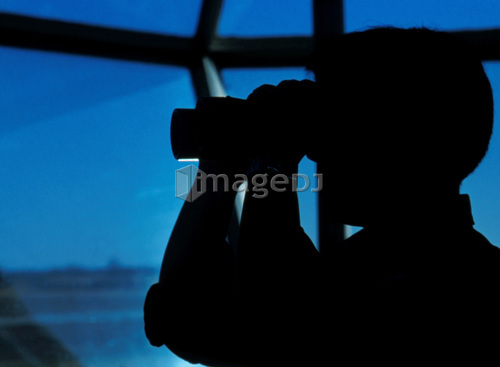A Navy air traffic controller maintains an alert watch with binoculars in the control tower.