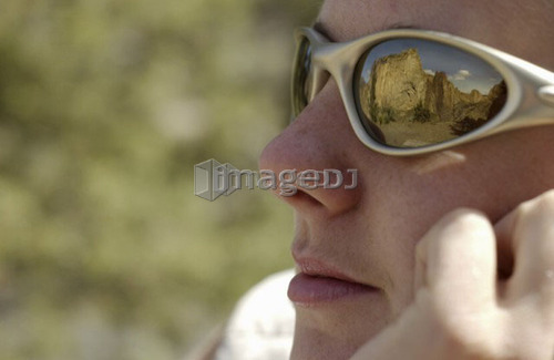 Woman (20-25) looking at rock cliffs with reflection of the cliffs in her sunglass lens, Smith Rock State Park, Oregon