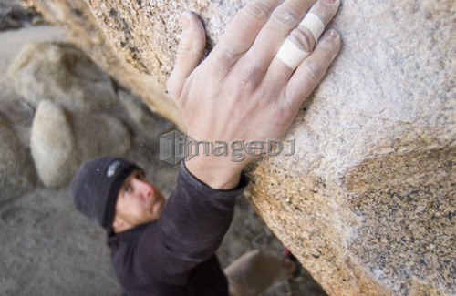 Man (25-30) rock climbing holding onto a sloping hand hold, Bishop, California