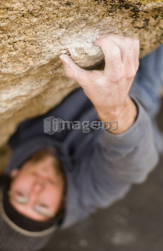 Man (20-25) clinging to a small handhold while rock climbing, Bishop, California