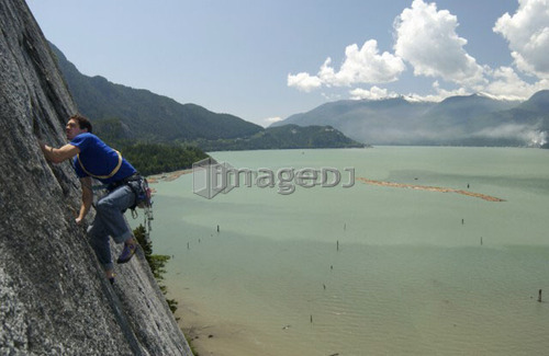 Man (20-25) climbing a rock face above the ocean, Squamish, B.C.