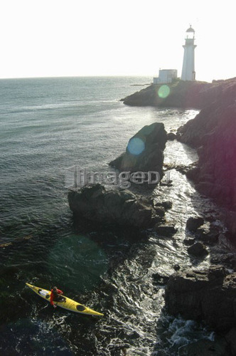 Man (30-35) kayaking in front of a lighthouse, Jordan River, B.C.