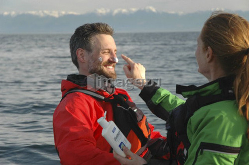 Man (30-35) and woman (25-30) sitting in kayaks applying sunscreen, Esquimalt, B.C.