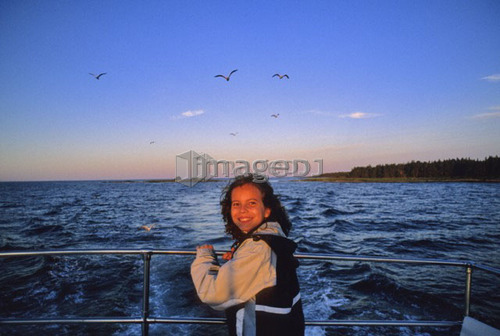Girl, 10, smiles, on boat with sunset and gulls behind, Nova Scotia