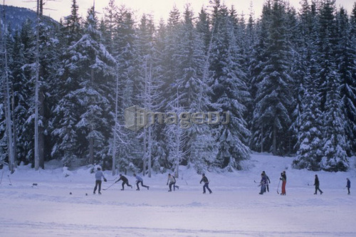 Men play hockey on mountain lake, winter late day, Whistler, B.C.