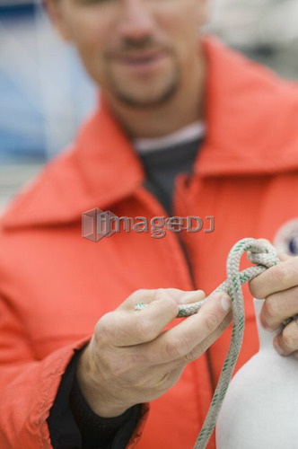 Man in marine rain/floatation gear tieing knot, Vancouver, B.C.
