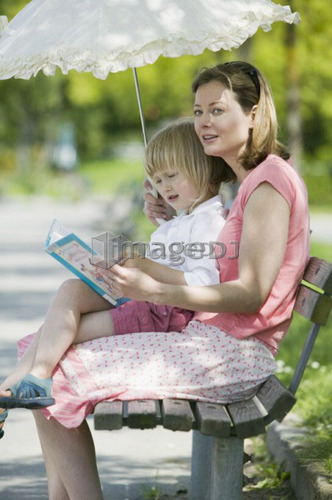 Caucasian Mom and 4 year old Daughter, reading a book on a park bench, Sunset Beach, Vancouver, B.C.