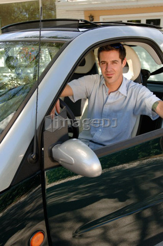 Young man sitting in smart car in front of house, Regina, Saskatchewan
