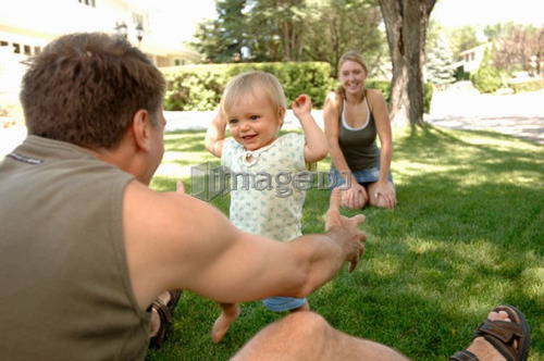 Young man & woman teaching baby to walk in grass, Regina, Saskatchewan