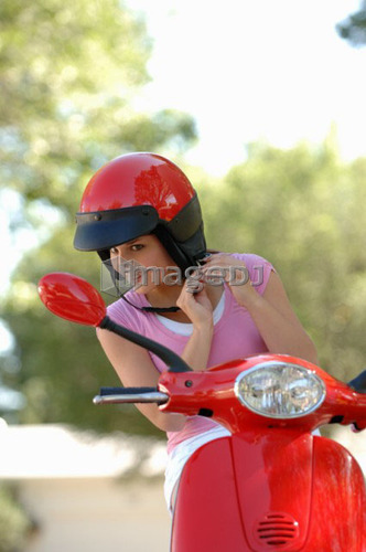 Young girl fastening helmet on red vespa, Regina, Saskatchewan