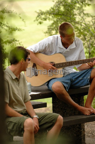 Young guys playing guitar sitting at picnic table, Regina, Saskatchewan