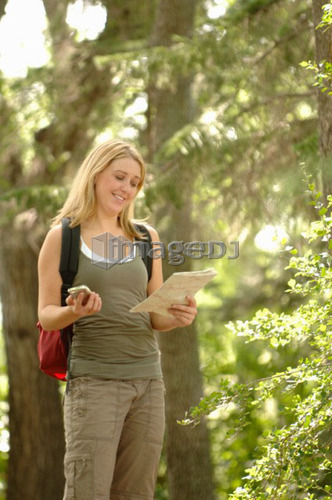 Young woman with gps type device and map in woods, Regina, Saskatchewan