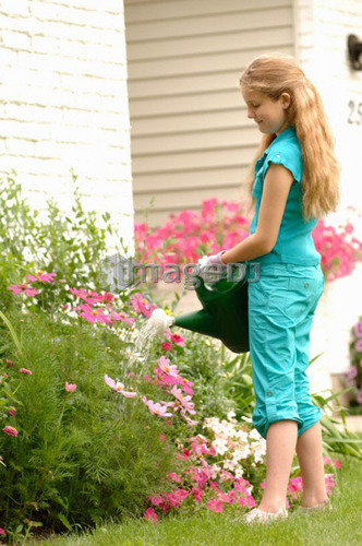 Young girl watering flowers in front of house, Regina, Saskatchewan