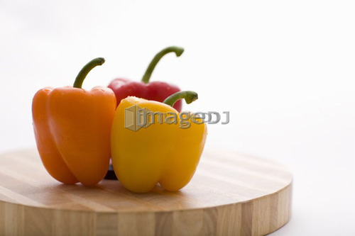 Yellow, orange and red peppers on butcher block cutting board in profile