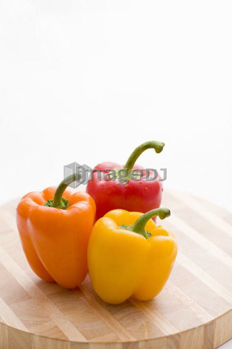 Yellow, orange and red peppers on butcher block cutting board