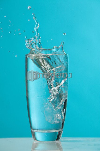 Water splash as ice cube drops into glass of water