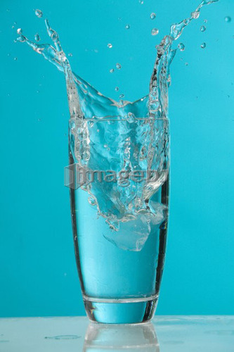 Water splash as ice cube drops into glass of water
