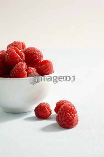 3 raspberries sit beside bowl of raspberries