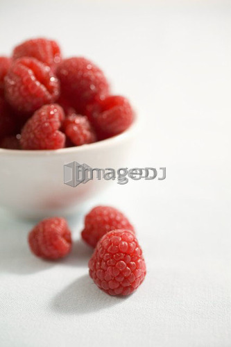 3 raspberries sit beside bowl of raspberries