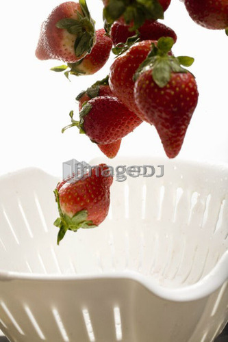 Strawberries falling into colander