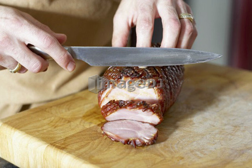 Oven roasted ham being sliced on cutting board with large knife