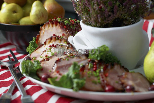 Festive oven roasted ham sliced and garnished with chives and cranberries accompanied by a bowl of pears and the Heather plant