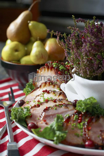 Festive oven roasted ham sliced and garnished with chives and cranberries accompanied by a bowl of pears and the Heather plant