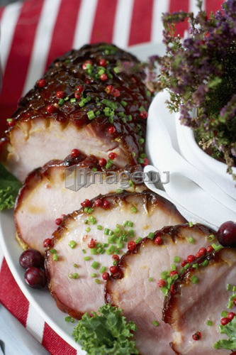 Festive oven roasted ham sliced and garnished with chives and cranberries