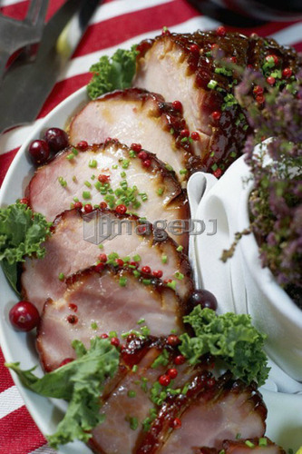 Festive oven roasted ham sliced and garnished with chives and cranberries