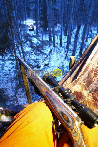 Rifle rests on knee of hunter, ATV approaching in distance, Alberta