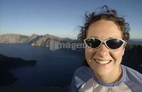 Woman (20-25) with sunglasses in front of lake and mountains, Crater Lake National Park, Oregon
