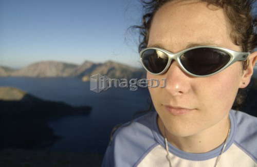 Woman (20-25) with sunglasses in front of lake and mountains, Crater Lake National Park, Oregon