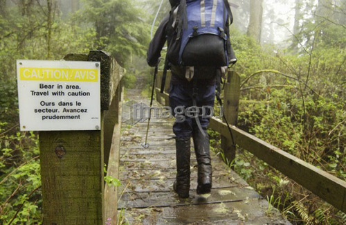 Backpacker walking past a sign saying Bear in Area, West Coast Trail, Pacific Rim National Park Reserve, BC