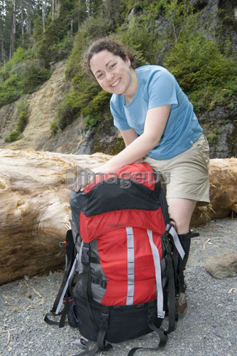 Woman (20-25) packing a large backpack on a beach with a large beach log in the background, West Coast Trail, Pacific Rim Nation