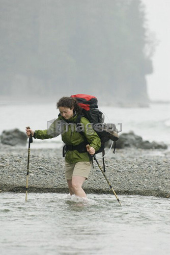 Woman (20-25) crossing a fast-flowing creek with a large backpack on, West Coast Trail, Pacific Rim National Park Reserve, BC