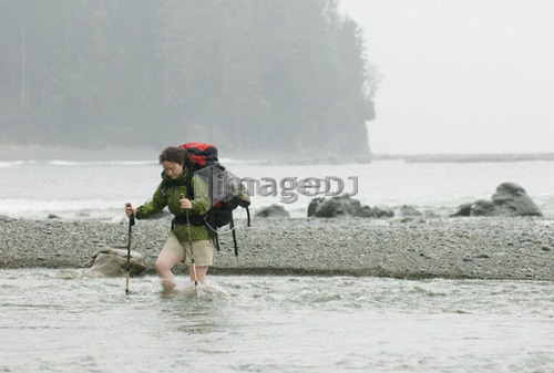 Woman (20-25) crossing a fast-flowing creek with a large backpack on, West Coast Trail, Pacific Rim National Park Reserve, BC