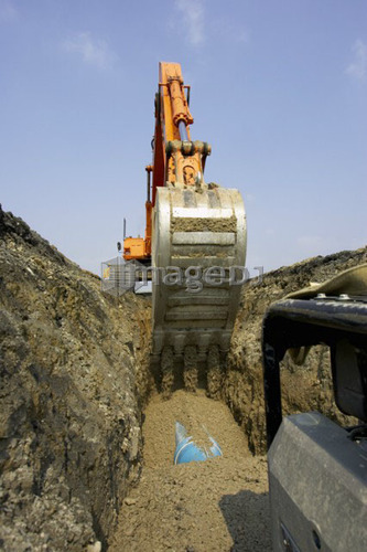 Excavator filling in section of drainage pipe with dirt; Canada, Ontario, Hamilton (Composting Facility)