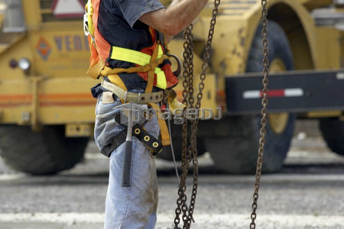 Construction worker in harness and tool belt adjusting chains; Canada, Ontario, Hamilton (Composting Facility)