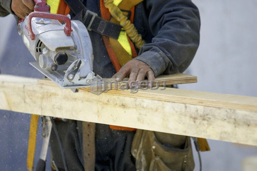 Construction worker cutting a piece of wood with a skill saw.; Canada, Ontario, Hamilton (Composting Facility)