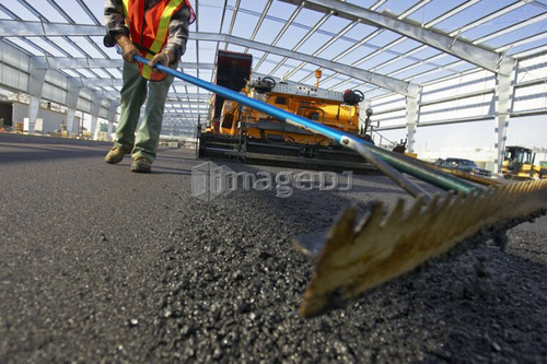 Worker leveling asphalt with a rake; Canada, Ontario, Hamilton (Composting Facility)
