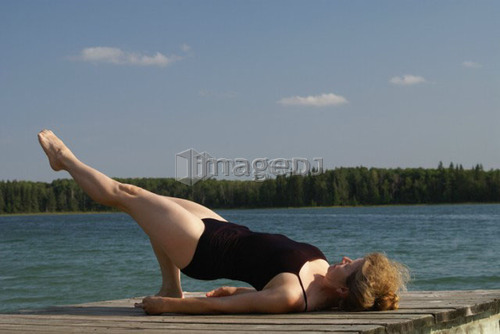 45 year old woman doing yoga on dock, no motors allowed on lake.; Canada, Manitoba, Riding Mountain National Park