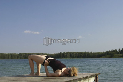 45 year old woman doing yoga on dock, no motors allowed on lake.; Canada, Manitoba, Riding Mountain National Park