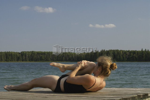 45 year old woman doing yoga on dock, no motors allowed on lake.; Canada, Manitoba, Riding Mountain National Park
