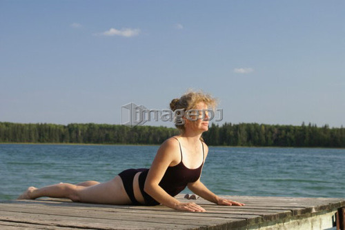 45 year old woman doing yoga on dock, no motors allowed on lake.; Canada, Manitoba, Riding Mountain National Park