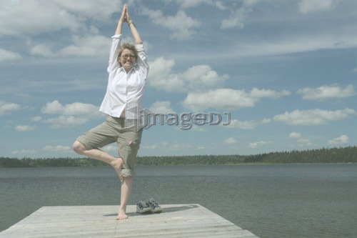 Woman in yoga pose on dock, Clear Lake; Canada, Manitoba, Riding Mountain National Park