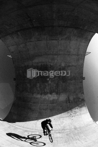 Black and white mountain biker dwarfed by concrete pipe; Canada, Alberta, Calgary, Shaw Millenium Park