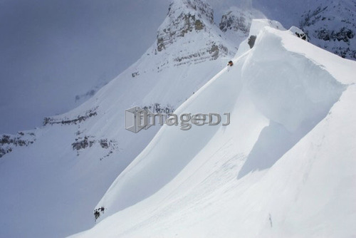 Skier on crest of big drop, dwarfed by mountain; Canada, British Columbia, Icefall Lodge