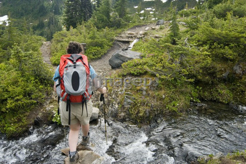 Woman crossing a small alpine creek; USA, Washington, Olympic National Park,