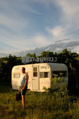 Man with briefcase stands in front of dumpy trailor; Canada, Saskatchewan, Regina