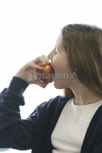 Pre-teen girl eating organic apple, wearing hoodie made with hemp fibre, Canada, Manitoba, Brandon